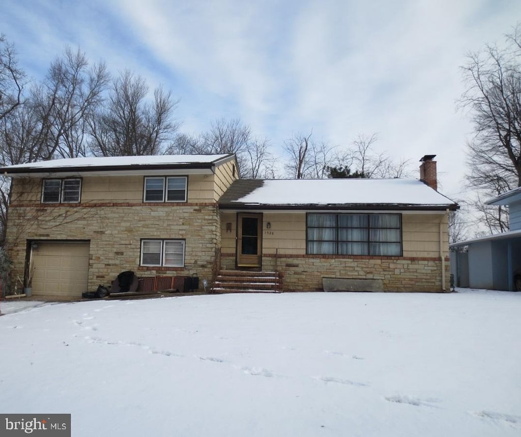 split level home featuring stone siding, a chimney, and an attached garage