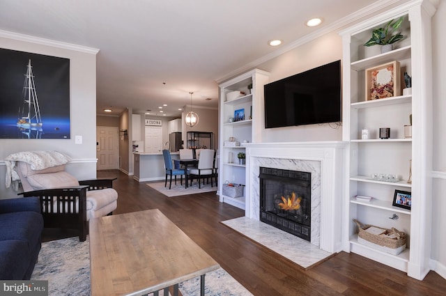 living room featuring a chandelier, crown molding, a premium fireplace, dark wood-type flooring, and built in shelves