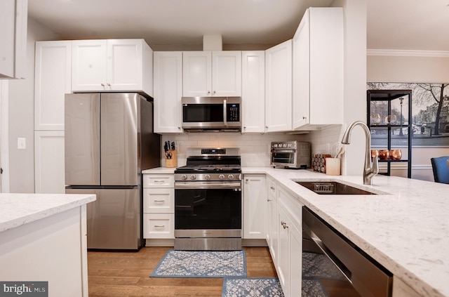 kitchen featuring sink, appliances with stainless steel finishes, light stone countertops, light hardwood / wood-style floors, and white cabinets