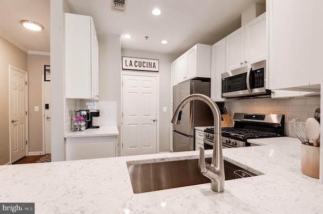 kitchen with appliances with stainless steel finishes, white cabinetry, decorative backsplash, light stone counters, and crown molding