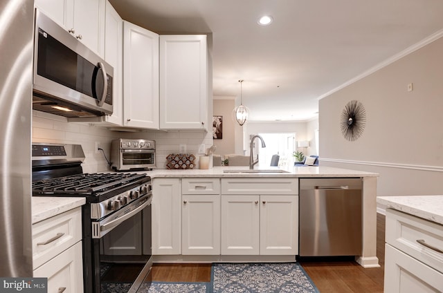 kitchen with white cabinetry, crown molding, appliances with stainless steel finishes, pendant lighting, and light stone countertops