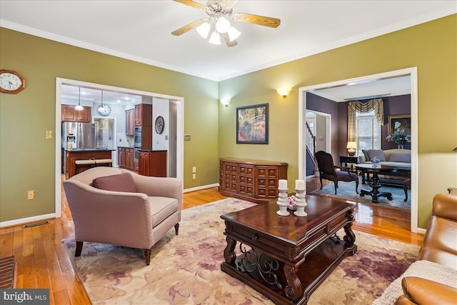 living room with ornamental molding, ceiling fan, and light wood-type flooring