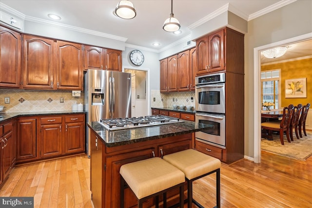 kitchen with decorative light fixtures, appliances with stainless steel finishes, a kitchen breakfast bar, a kitchen island, and dark stone counters