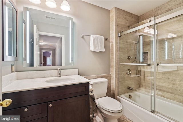 full bathroom featuring toilet, vanity, bath / shower combo with glass door, and tile walls