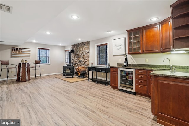 kitchen with sink, a wood stove, beverage cooler, dark stone counters, and light hardwood / wood-style flooring