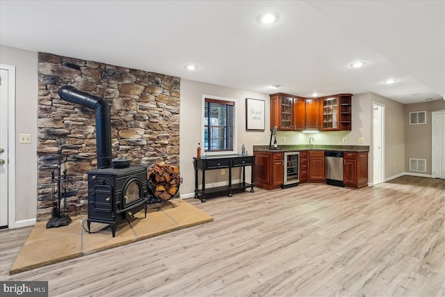 interior space with sink, light hardwood / wood-style flooring, a wood stove, stainless steel dishwasher, and beverage cooler