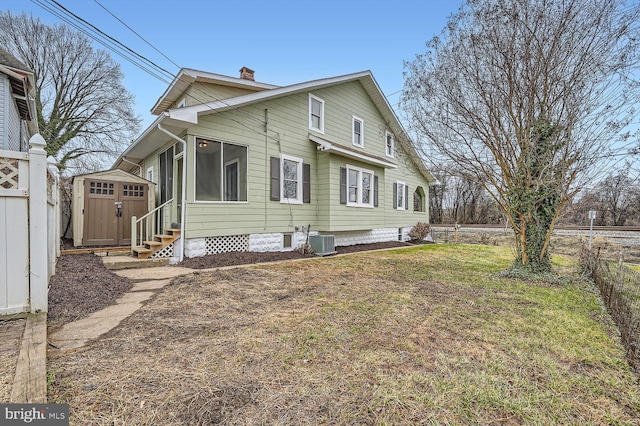 back of house featuring central AC, a lawn, and a storage unit