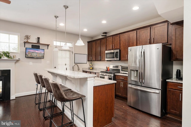 kitchen with dark wood-type flooring, a kitchen island with sink, stainless steel appliances, light stone counters, and decorative light fixtures