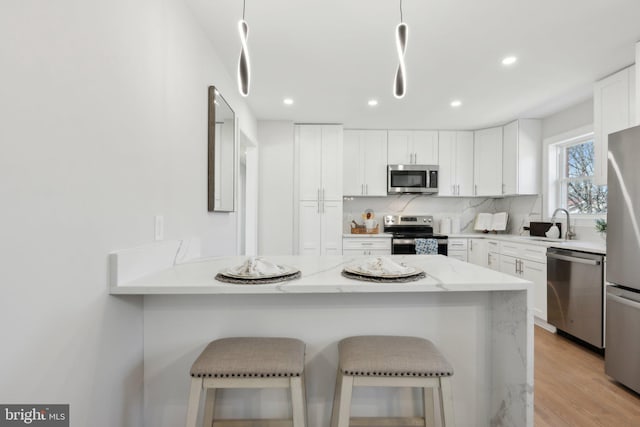 kitchen featuring light stone countertops, appliances with stainless steel finishes, white cabinets, and a breakfast bar area