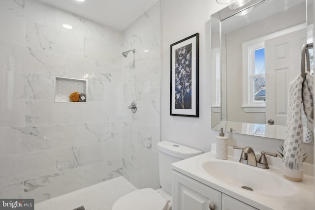 bathroom with a tile shower, vanity, and toilet