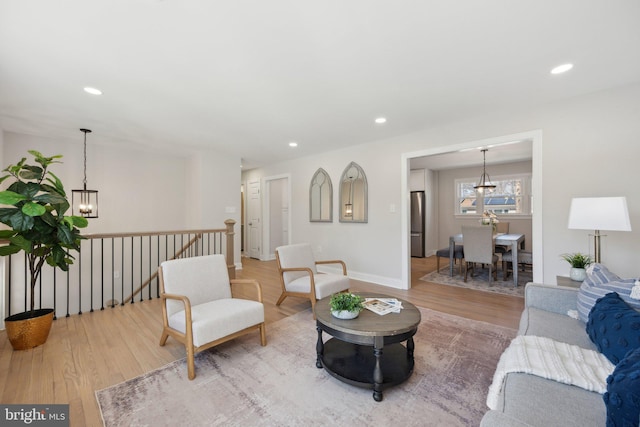 living area with light wood-type flooring, a notable chandelier, baseboards, and recessed lighting