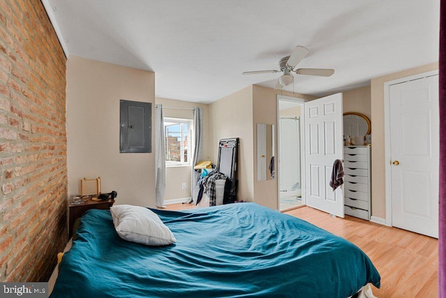 bedroom with wood-type flooring, electric panel, ceiling fan, and brick wall