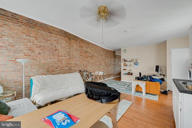 interior space featuring light hardwood / wood-style floors, ceiling fan, and brick wall