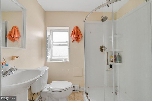 bathroom with a shower with shower door, sink, baseboard heating, toilet, and tile patterned floors