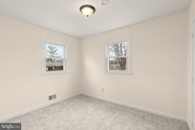 carpeted empty room featuring a healthy amount of sunlight, baseboards, and visible vents