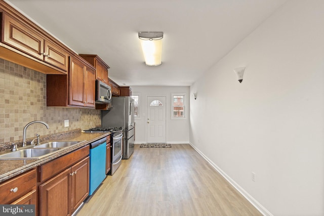 kitchen with appliances with stainless steel finishes, backsplash, a sink, and light wood-style flooring