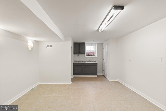 basement with light tile patterned floors, a sink, visible vents, and baseboards