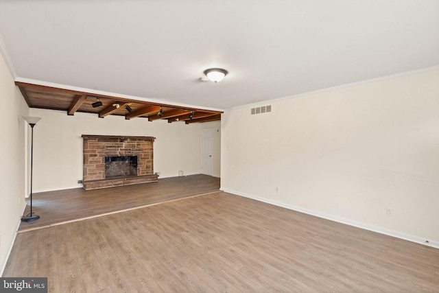 unfurnished living room with crown molding, visible vents, a stone fireplace, wood finished floors, and beamed ceiling