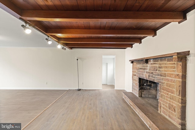 unfurnished living room featuring baseboards, wooden ceiling, beamed ceiling, wood finished floors, and a stone fireplace