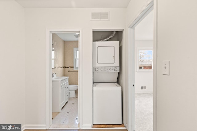 washroom featuring light tile patterned floors, stacked washer / dryer, a sink, and visible vents