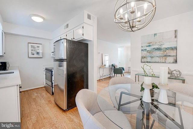 kitchen with light hardwood / wood-style flooring, white cabinetry, stainless steel appliances, decorative light fixtures, and a chandelier