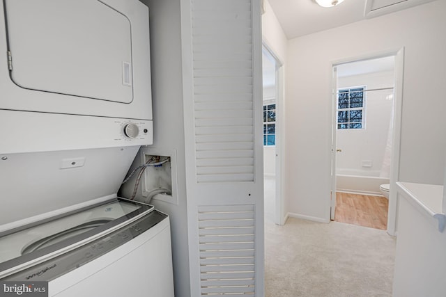 washroom featuring stacked washer and clothes dryer and light carpet