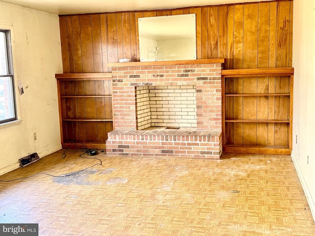 unfurnished living room with a brick fireplace, wooden walls, and light parquet floors