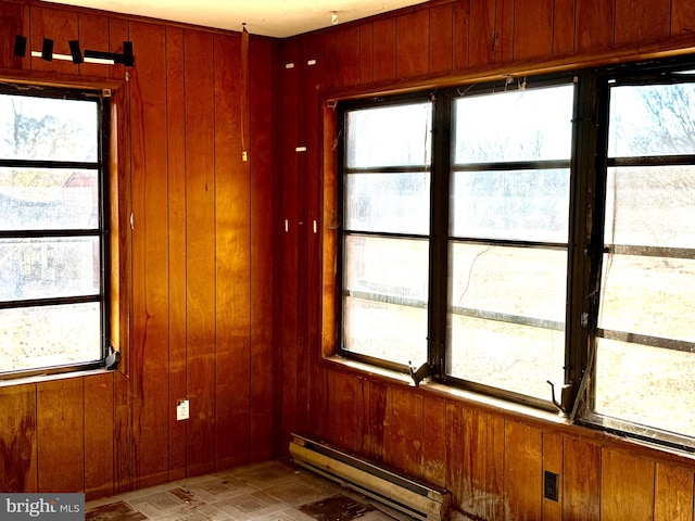 unfurnished room with a baseboard heating unit, wooden walls, and plenty of natural light