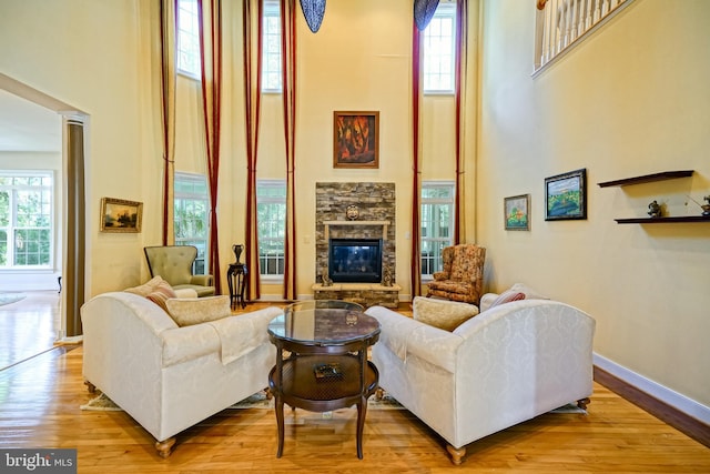 living area with a stone fireplace, wood finished floors, a towering ceiling, baseboards, and ornate columns