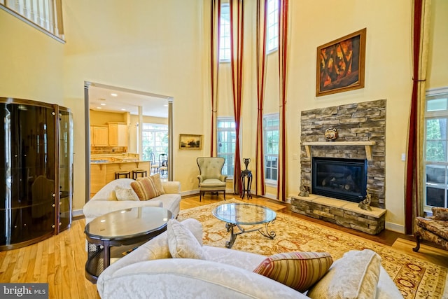 living room featuring plenty of natural light, a stone fireplace, a high ceiling, and wood finished floors