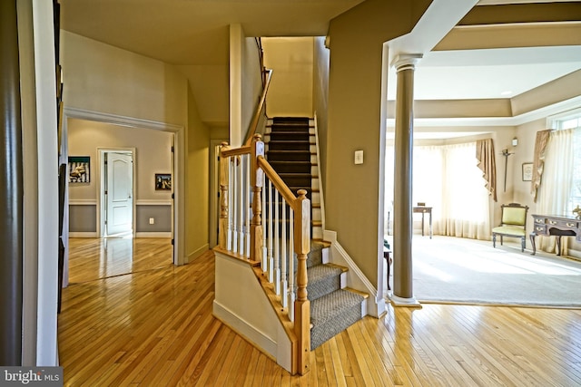 staircase with baseboards, hardwood / wood-style floors, and ornate columns