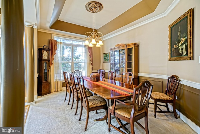 dining space with light carpet, wainscoting, an inviting chandelier, a raised ceiling, and crown molding