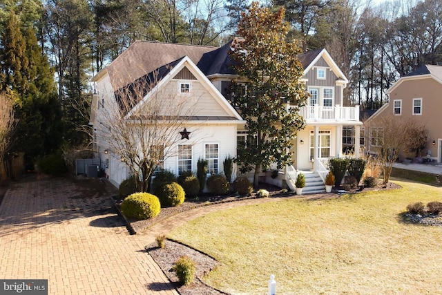 view of front facade featuring a balcony, decorative driveway, central air condition unit, a front lawn, and board and batten siding