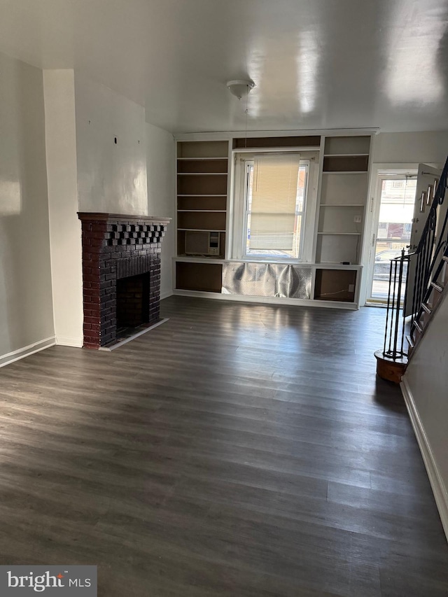 unfurnished living room featuring a brick fireplace, dark wood-type flooring, and built in shelves