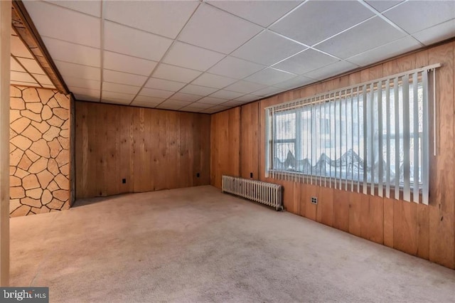 unfurnished room with a drop ceiling, radiator, carpet floors, and wood walls