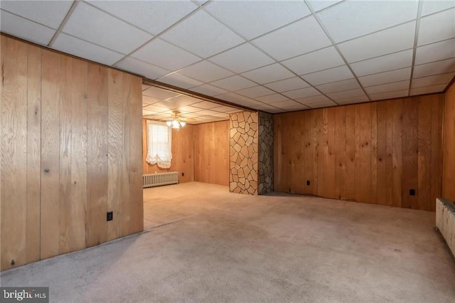 basement with a paneled ceiling, radiator, light carpet, and wood walls