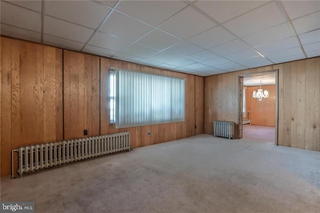 carpeted spare room featuring a paneled ceiling, wooden walls, and radiator