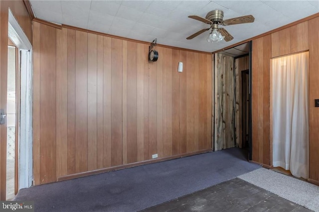 carpeted spare room featuring wooden walls and ceiling fan