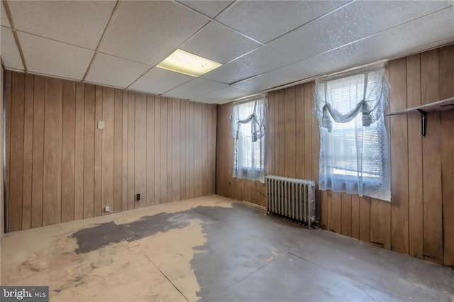 spare room with radiator heating unit, a drop ceiling, concrete floors, and wood walls