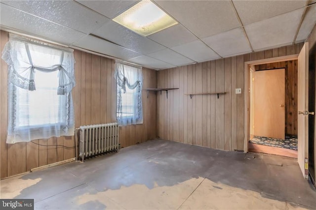 spare room with a paneled ceiling, radiator heating unit, concrete flooring, and wood walls