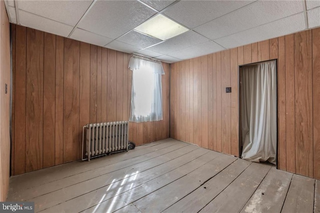 spare room featuring radiator, a drop ceiling, light hardwood / wood-style floors, and wood walls