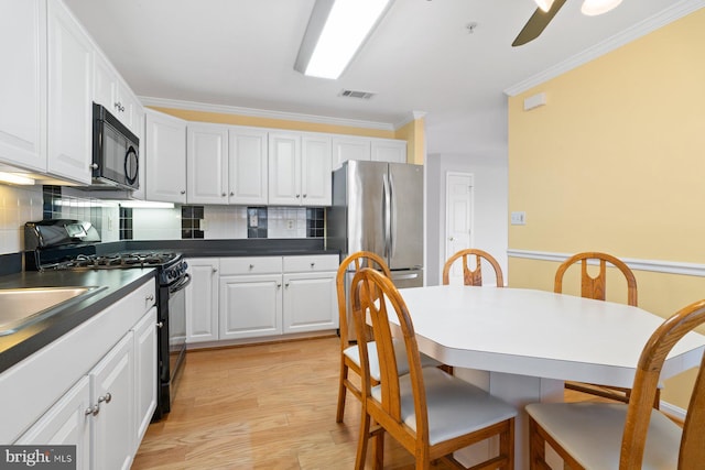 kitchen with dark countertops, visible vents, ornamental molding, white cabinetry, and black appliances