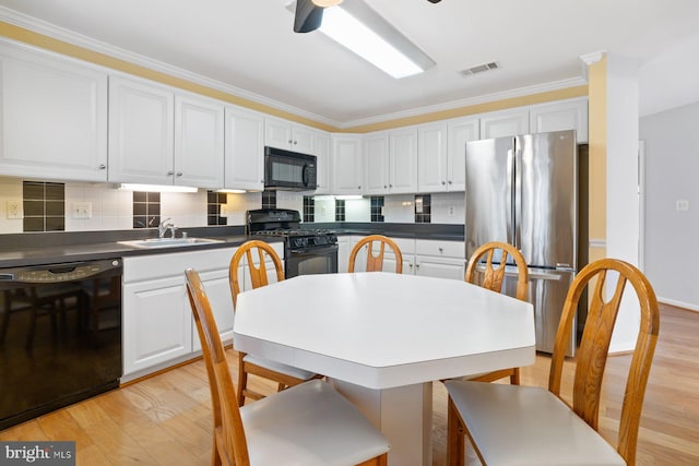 kitchen featuring a sink, visible vents, white cabinetry, light wood-type flooring, and black appliances