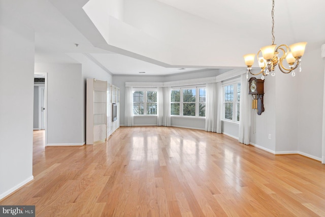 unfurnished living room with a notable chandelier, light wood-type flooring, and baseboards