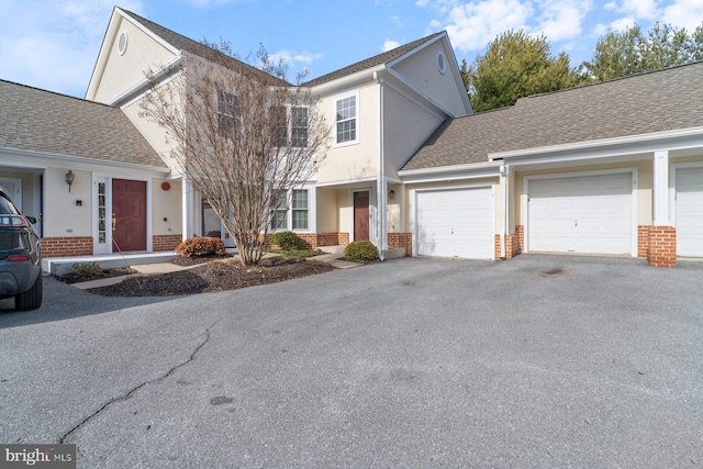 view of front of property featuring an attached garage, brick siding, driveway, roof with shingles, and stucco siding