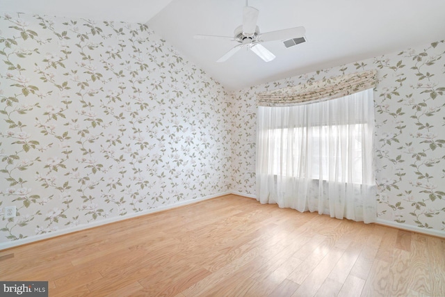 unfurnished room with lofted ceiling, visible vents, light wood finished floors, and wallpapered walls