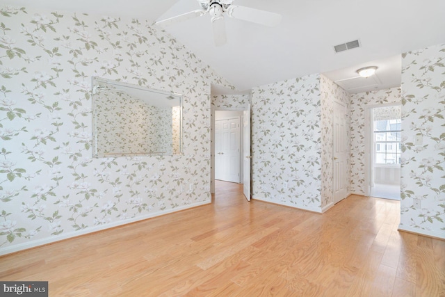 spare room with wallpapered walls, baseboards, visible vents, wood finished floors, and vaulted ceiling