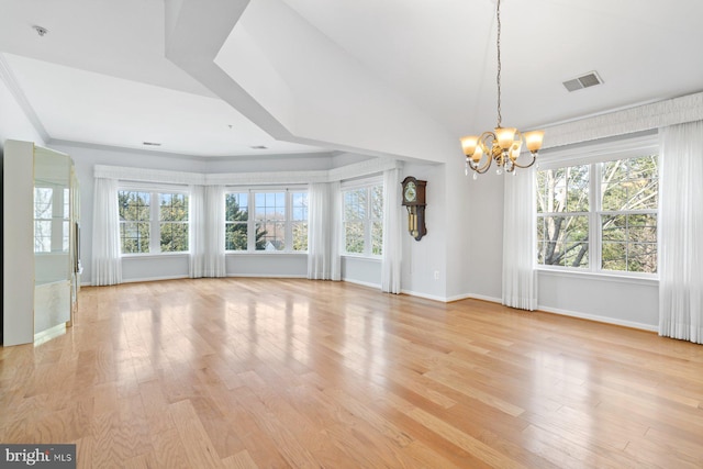 empty room featuring a wealth of natural light, light wood-type flooring, a chandelier, and visible vents