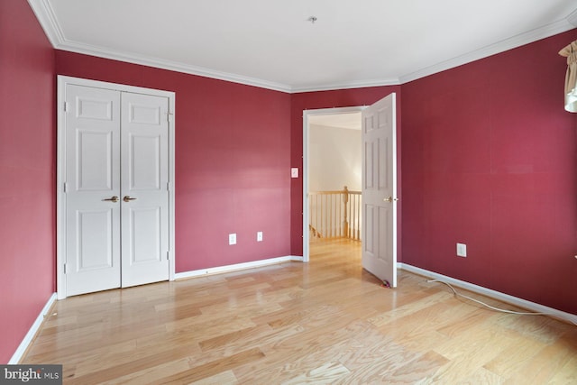 unfurnished bedroom with crown molding, light wood finished floors, a closet, and baseboards