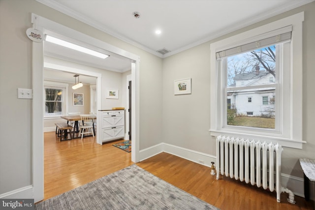 hall featuring hardwood / wood-style flooring, ornamental molding, radiator, and a wealth of natural light